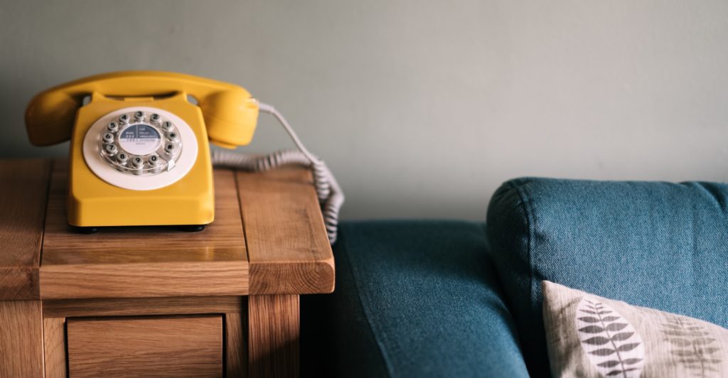 Yellow rotary phone next to blue sofa photo by Annie Spratt from Unsplash